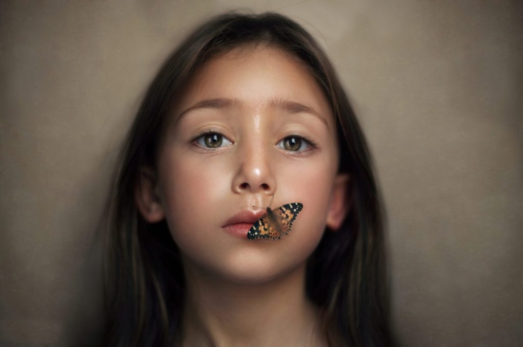 Niña con mariposa posada en los labios